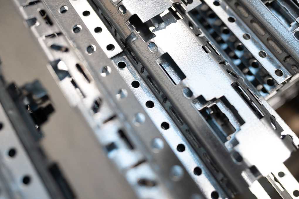 Nærbilde av metalliske metallrammer og deler som utgjør en datamaskins hovedkort, med mange hull og spor for komponenter.