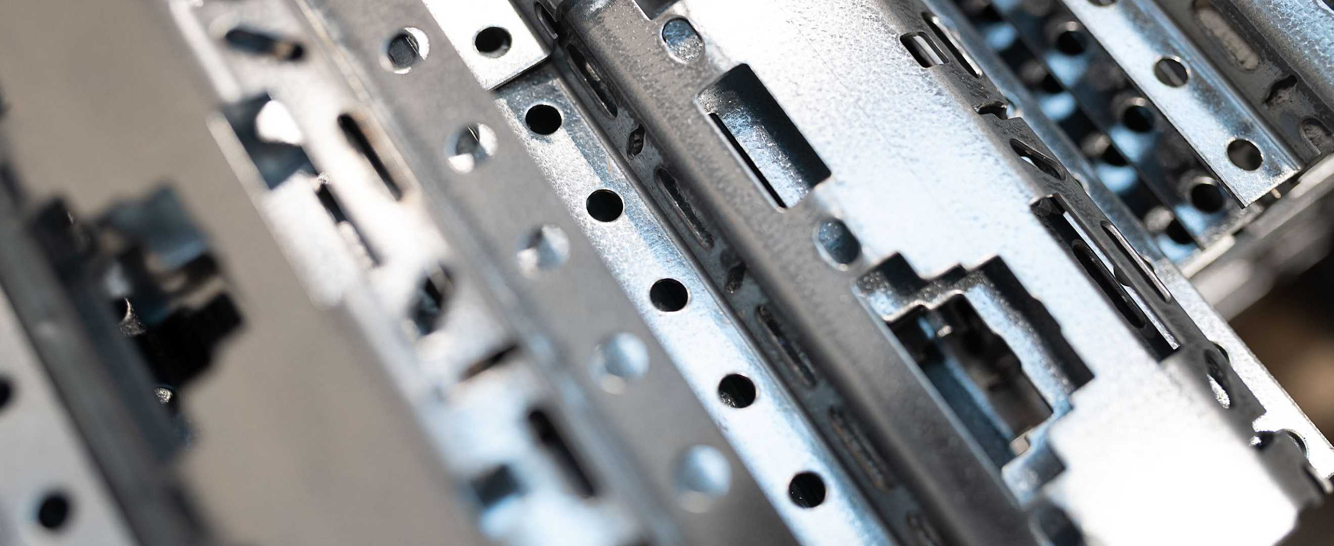 Nærbilde av metalliske metallrammer og deler som utgjør en datamaskins hovedkort, med mange hull og spor for komponenter.