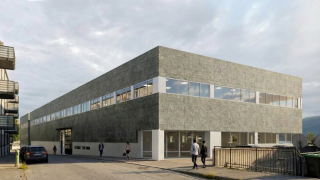 Selve bygningen har en moderne, firkantet design med store vindusrekker langs midten, omgitt av en åpen uterom med noen menneske og biler.